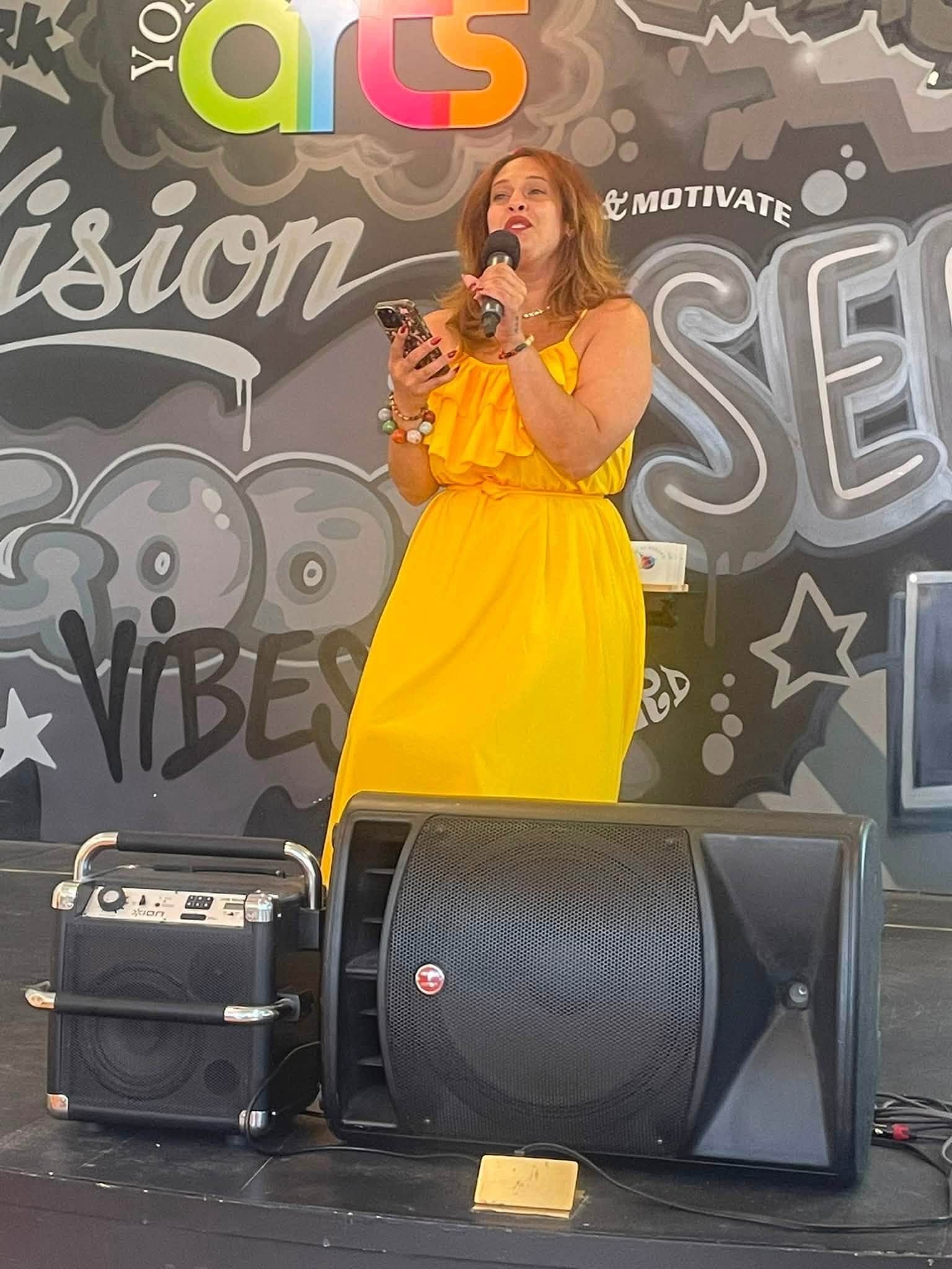 Woman in yellow dress singing on stage at Yonkers Arts
